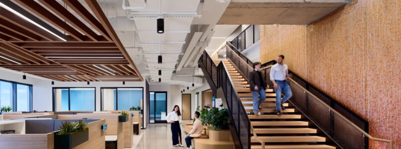 Open office with wood ceiling baffles, workstations and a feature staircase in the Simpson Strong-Tie office