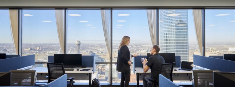Colleagues talking among blue workstations with panoramic city views in the AT&T office