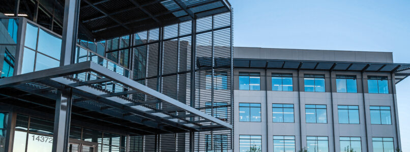 Modern glass and steel office building entrance with a metal canopy at sunset