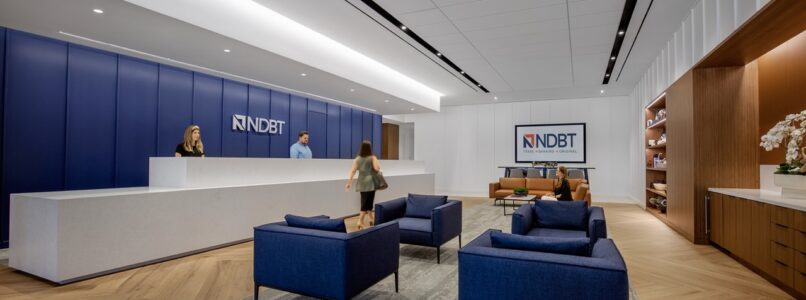 NDBT reception area with white desk, blue lounge chairs and logo wall
