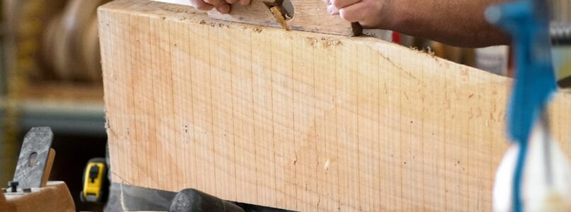 Carpenter using a hand plane on a block of wood at a workbench with tools