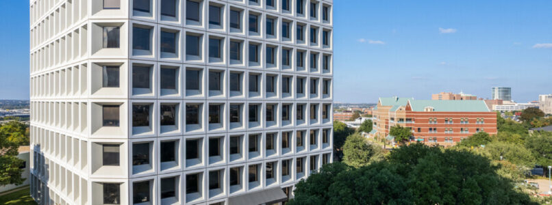 Modern white grid-facade office building surrounded by trees under a blue sky