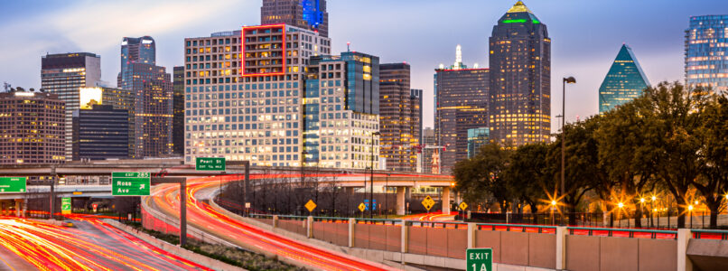 Dallas skyline at dusk above a highway with light trails