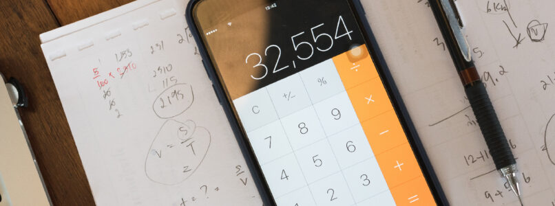 Smartphone calculator and pencil on paper covered with handwritten calculations