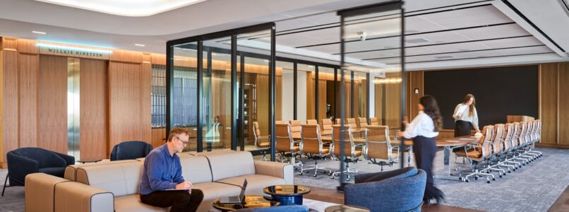 Open lounge with sofas and armchairs next to a glass-walled conference room in the Willkie Dallas office